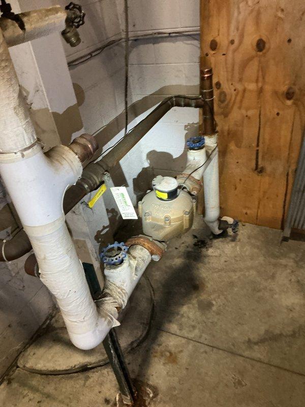 Responded to water leak originating from the city water main connection to the customer's private service line. Upon inspection, located the leak at the transition point between municipal infrastructure and residential plumbing system near the water meter assembly in the basement utility area. Assessed the existing plumbing configuration, including PVC piping, copper connections, and meter housing with shutoff valves. Investigated the outdoor service line path from the street to the residence, examining the drainage area and identifying potential points of water intrusion. Documented existing conditions of the water meter installation, valve assemblies, and associated piping infrastructure showing age-related wear and oxidation. Evaluated the extent of water damage on the concrete basement floor and determined the source of the leak for repair recommendations.