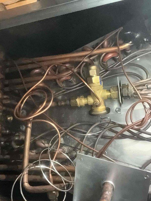Responded to no-cooling call on 1-year-old attic-mounted air conditioning system experiencing complete failure, identified as repeat issue from previous service. Diagnosed faulty thermostatic expansion valve (TXV) preventing refrigerant flow and system operation. Ordered replacement TXV-3T-454 component from shop inventory for R410A system rated at 670 psig MWP. Documented existing copper refrigerant line configuration, valve assembly, and system components via photos for warranty documentation and future reference.