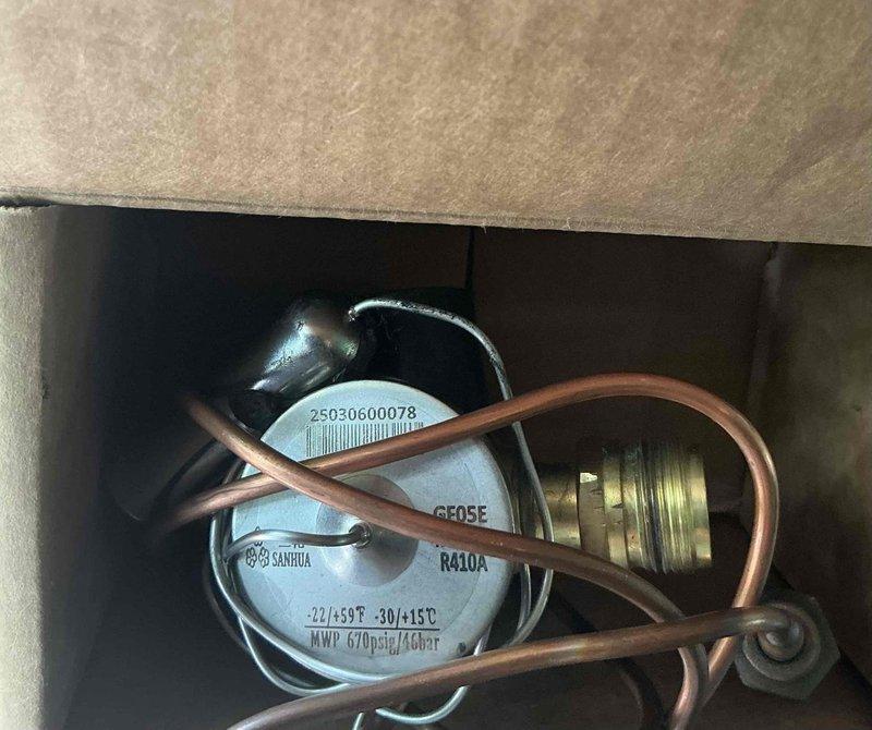 Responded to no-cooling call on 1-year-old attic-mounted air conditioning system experiencing complete failure, identified as repeat issue from previous service. Diagnosed faulty thermostatic expansion valve (TXV) preventing refrigerant flow and system operation. Ordered replacement TXV-3T-454 component from shop inventory for R410A system rated at 670 psig MWP. Documented existing copper refrigerant line configuration, valve assembly, and system components via photos for warranty documentation and future reference.