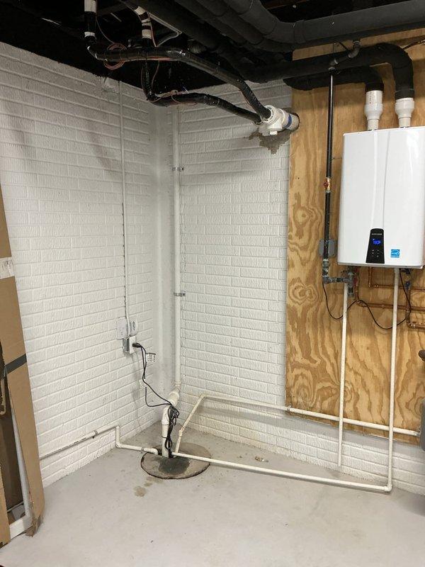 Installed water-powered backup sump pump system with RPZ (Reduced Pressure Zone) backflow preventer in basement utility area. The installation included routing white PVC discharge piping vertically from floor level, connecting to existing plumbing infrastructure, and ensuring proper integration with the home's water supply system to provide automatic backup pumping capability during primary pump failure or power outages.