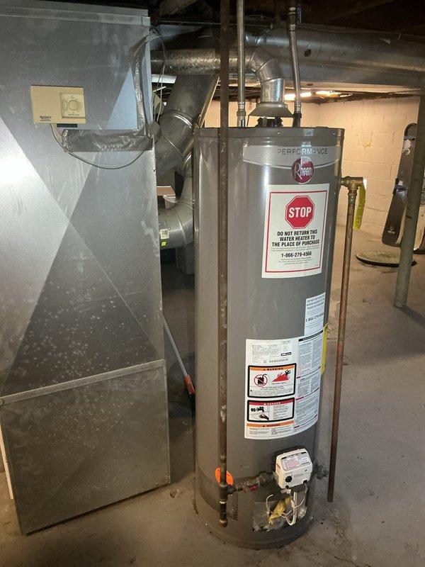 Responded to report of water heater leaking and possible leak from upstairs bathroom. Upon inspection, located a Rheem Performance gas water heater in basement utility area manufactured in March 2018. Conducted thorough visual examination of the unit, including all copper piping connections at top and bottom, gas valve assembly, and tank exterior for signs of moisture or corrosion. Documented existing conditions of water heater installation and surrounding plumbing connections. Assessed potential leak sources and verified unit specifications and safety compliance labels were intact and legible.