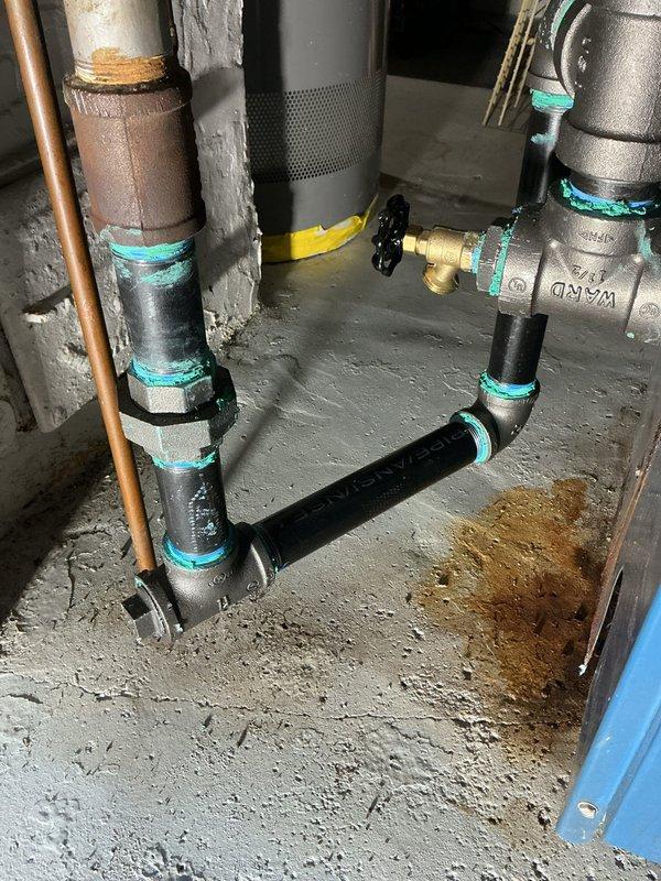 # Boiler System Repair and Component Replacement

Responded to service call for boiler system requiring repairs. Upon inspection, identified aging plumbing connections with visible corrosion and deterioration on copper and brass fittings, particularly noting green patina formation indicating oxidation on metal components.

Performed comprehensive repairs to the blue-cased boiler unit's piping system. Replaced deteriorated pipe sections and installed new turquoise-colored rubber couplings to ensure proper sealing and prevent future leaks. Addressed corroded vertical pipes running along the left side of the unit that showed significant wear and surface weathering.

Installed new gas shutoff valve assembly with yellow handle for improved safety and accessibility. Connected valve to gray metal pipes using turquoise compression fittings to ensure secure, leak-free connections. Replaced aging black plastic pipe sections that exhibited brown discoloration and signs of degradation.

Inspected 