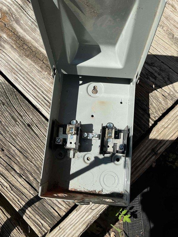 Responded to no cooling complaint on 6-year-old air conditioning system with equipment located in laundry room. Upon arrival, inspected outdoor electrical disconnect box and found evidence of fuse failure or electrical issue within the exterior disconnect panel. Photographed weathered disconnect box showing internal fuses, contactors, and wiring connections for documentation purposes. The disconnect box exhibited signs of outdoor weathering and age-related deterioration on exterior surfaces. Inspected internal electrical components including fuses, terminals, and wire connections to diagnose power supply issue preventing compressor operation. Identified faulty or blown fuses as likely cause of no cooling condition, preventing power from reaching outdoor condensing unit.