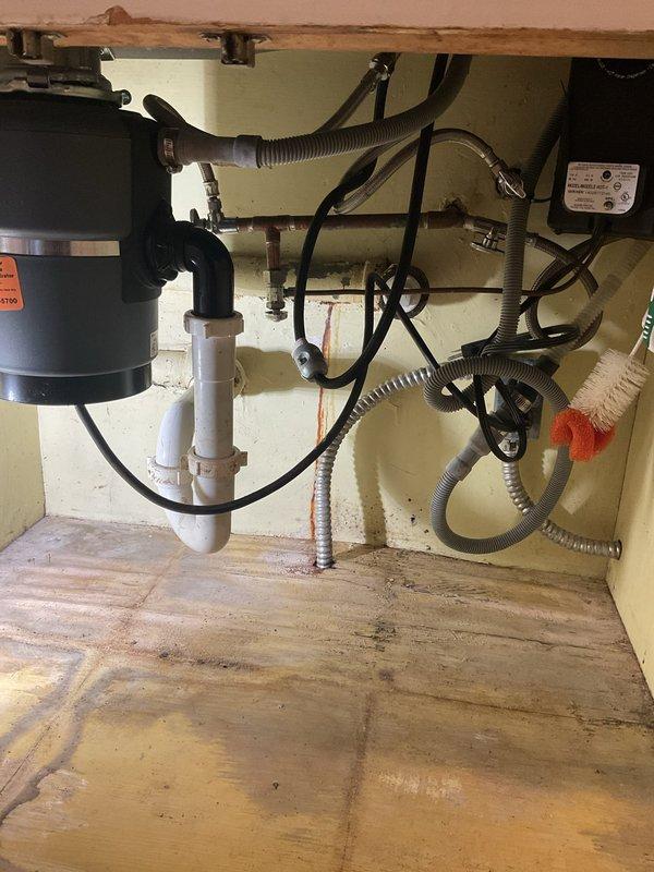 Responded to service call for kitchen sink leak originating from beneath the basin. Upon inspection of the cabinet interior, identified water damage on cabinet floor and examined all plumbing connections including garbage disposal unit, drain assembly, and supply lines. Inspected stainless steel double-basin sink with pull-out faucet and soap dispenser for source of leak. Evaluated all visible PVC drain pipes, flexible supply hoses, and disposal connections for signs of moisture, loose fittings, or deteriorated seals.