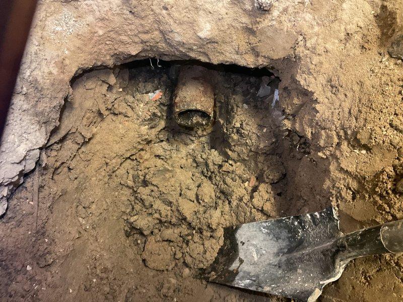 Completed floor break per estimate to access underground plumbing system. Excavated concrete flooring to expose deteriorated piping infrastructure requiring repair. Removed damaged section of floor slab, revealing corroded horizontal pipe within cavity. Documented existing conditions showing significant deterioration of both concrete foundation and exposed metallic piping components with visible rust and corrosion. Work included breaking through concrete surface, creating access point for necessary plumbing repairs to underground utilities.
