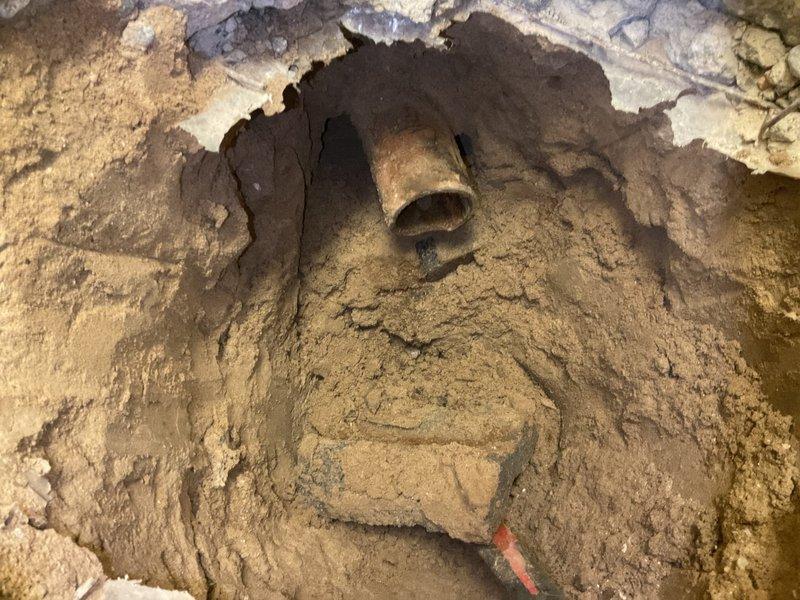 Completed floor break per estimate to access underground plumbing system. Excavated concrete flooring to expose deteriorated piping infrastructure requiring repair. Removed damaged section of floor slab, revealing corroded horizontal pipe within cavity. Documented existing conditions showing significant deterioration of both concrete foundation and exposed metallic piping components with visible rust and corrosion. Work included breaking through concrete surface, creating access point for necessary plumbing repairs to underground utilities.