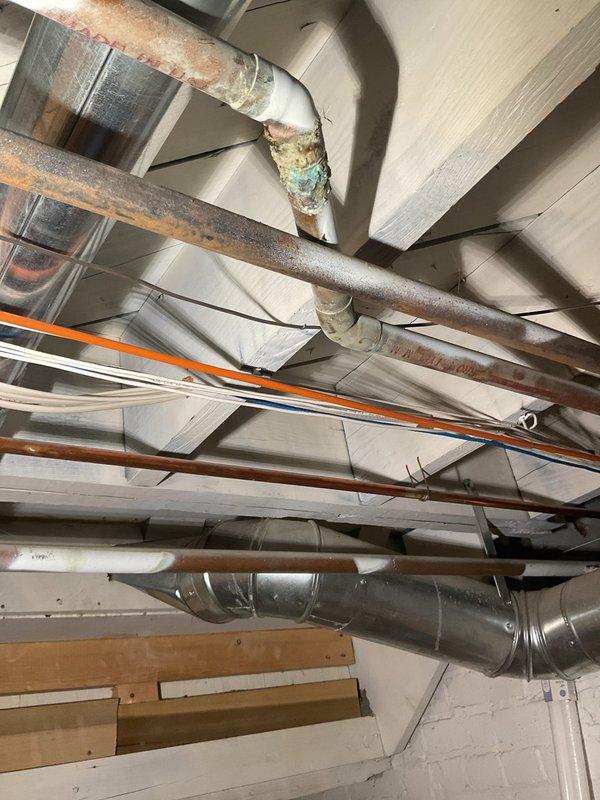 Responded to a shower leak that had been active for approximately two weeks, originating from a second-floor bathroom fixture and causing water damage to the first-floor ceiling below. Upon inspection of the exposed plumbing infrastructure in the basement area, identified severely corroded copper supply lines with visible oxidation, verdigris formation, and deterioration at multiple pipe joints. The aging plumbing system, consistent with the 80-year-old home's original installation, showed extensive wear including rust patches, compromised connections, and failing solder joints that were the source of the ongoing leak. Documented the condition of all visible copper piping, galvanized lines, and associated fittings throughout the affected area. The corroded sections exhibited characteristic turquoise and greenish discoloration indicating active copper degradation and moisture exposure over an extended period, which had allowed water to penetrate through to the living space below.