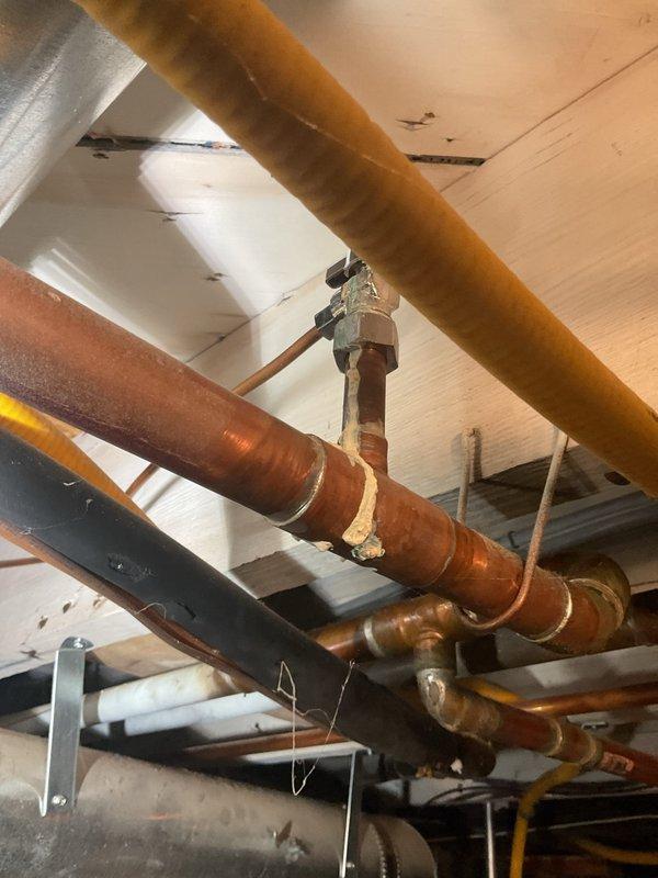 Responded to a shower leak that had been active for approximately two weeks, originating from a second-floor bathroom fixture and causing water damage to the first-floor ceiling below. Upon inspection of the exposed plumbing infrastructure in the basement area, identified severely corroded copper supply lines with visible oxidation, verdigris formation, and deterioration at multiple pipe joints. The aging plumbing system, consistent with the 80-year-old home's original installation, showed extensive wear including rust patches, compromised connections, and failing solder joints that were the source of the ongoing leak. Documented the condition of all visible copper piping, galvanized lines, and associated fittings throughout the affected area. The corroded sections exhibited characteristic turquoise and greenish discoloration indicating active copper degradation and moisture exposure over an extended period, which had allowed water to penetrate through to the living space below.
