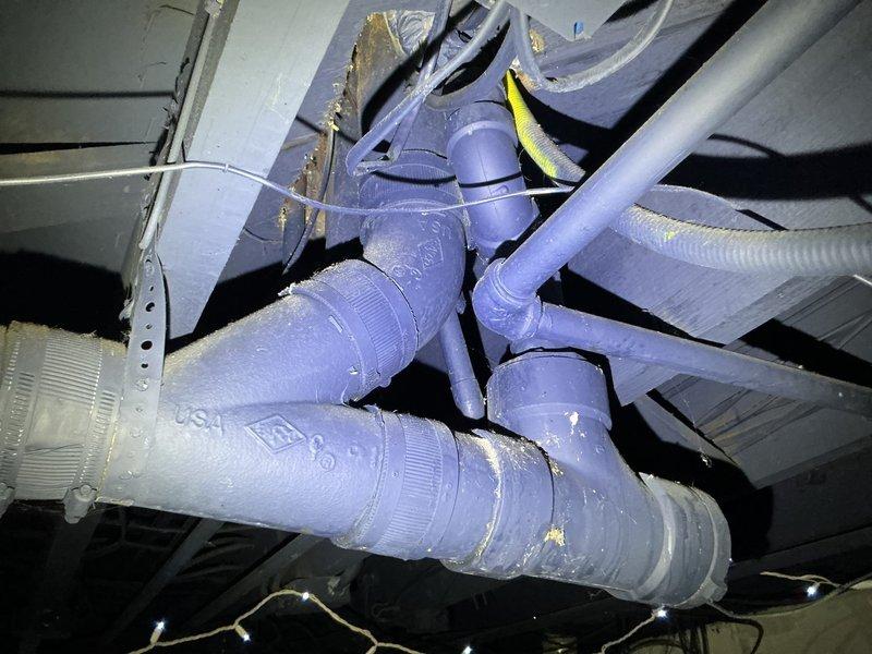 Responded to service call for malfunctioning toilet and drainage issue with waste backing up in pipes. Upon arrival, contacted customer regarding water main break outside property before proceeding with interior plumbing assessment. Investigated toilet malfunction and identified back pitch problem causing waste to accumulate in drainage line. Inspected underfloor plumbing assembly including PVC pipe connections, T-junction fittings, and drainage system configuration in basement utility area. Examined purple PVC piping network with multiple elbows, couplings, and flexible corrugated hoses to diagnose drainage flow issues. Addressed improper pipe slope preventing adequate waste evacuation through the system. Documented existing plumbing configuration and connection points for reference. Resolved toilet operational issues and corrected drainage concerns to restore proper waste flow.