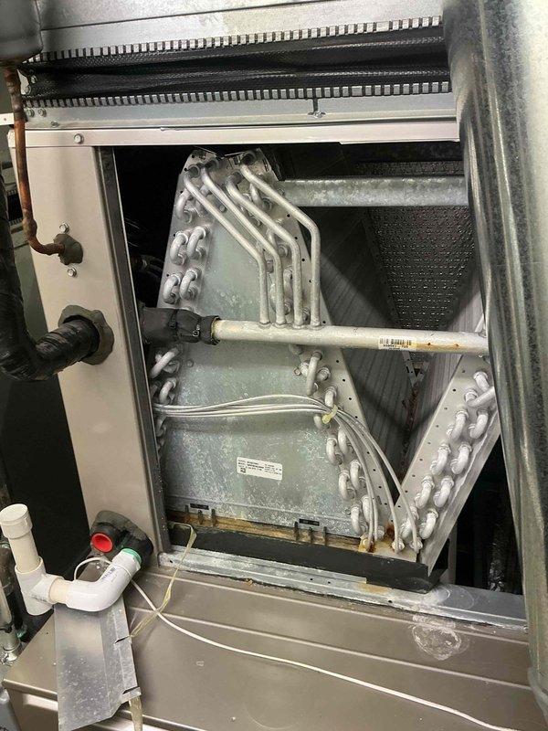 Responded to service call for leak search on CMVP4824AA4A4A air conditioning system manufactured in June 2015. Upon inspection, discovered significant white crystalline buildup and mineral deposits covering evaporator coil and metal surfaces, indicating prolonged refrigerant leak and moisture accumulation. Accessed interior evaporator coil assembly through service panel and documented extensive frosting on aluminum tube serpentine heat exchanger. Observed condensation on PVC drain lines with visible moisture present throughout system. Photographed equipment nameplate and internal components showing corrosion on mounting brackets and hardware. System required management consultation prior to presenting findings and repair recommendations to property owner due to extent of leak damage and potential need for coil replacement or major refrigerant system repairs.