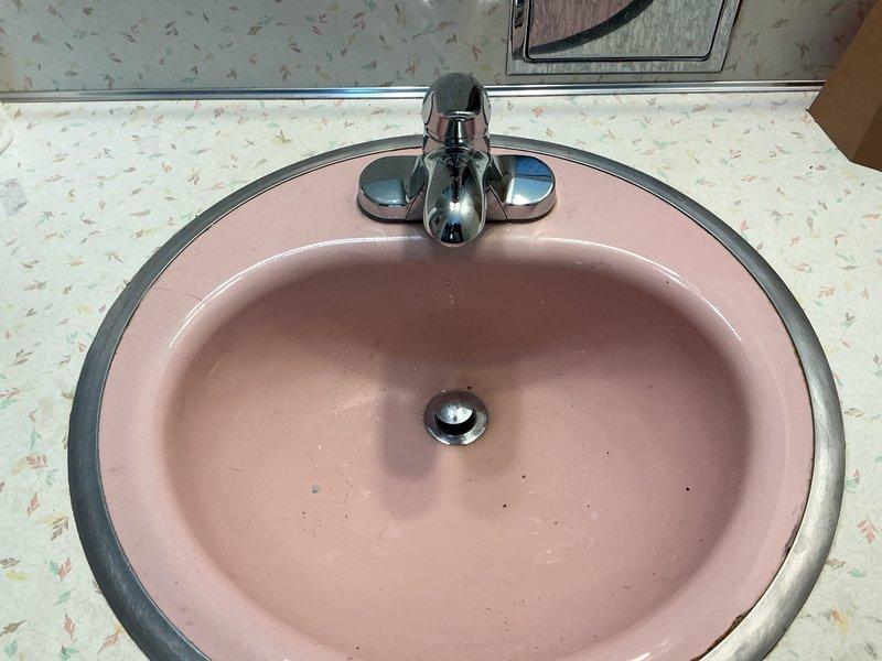 Installed new chrome two-handle faucet assembly on existing pink oval bathroom sink per customer estimate. Completed mounting of faucet with hot and cold water handles and central spout, ensuring proper connections and testing for leaks. All fixtures are operational and ready for use.