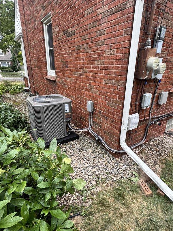 Completed full installation of 2.5-ton air conditioning system with new evaporator coil in right side yard location. Unit positioned on gravel pad against brick exterior wall with electrical disconnect box mounted above, refrigerant lines properly insulated and routed through wall, and all electrical conduit secured per code requirements. System reconnected, tested, and left operational with all mechanical, electrical, and air conditioning permits requested and processed.