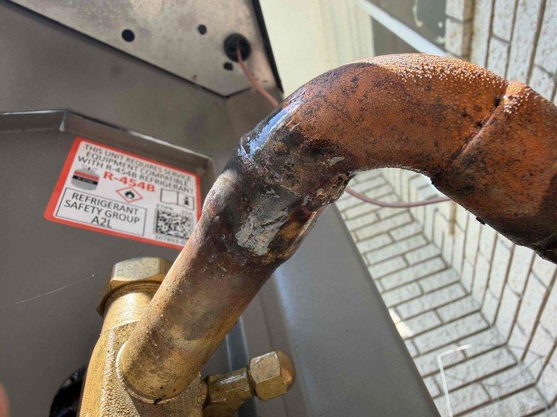 Returned to address refrigerant leak on copper elbow fitting of 7-month-old AC system located in basement. Upon inspection, discovered significant corrosion and active leak at curved copper refrigerant line with brass compression fitting, evidenced by moisture accumulation and rust deterioration on pipe surface. System was experiencing short cycling due to low refrigerant charge from leak, resulting in excessive compressor operation and increased energy consumption. Repaired leak at elbow connection, pressure tested system, evacuated lines, and recharged unit to manufacturer specifications. Verified proper system operation with normal run cycles restored.