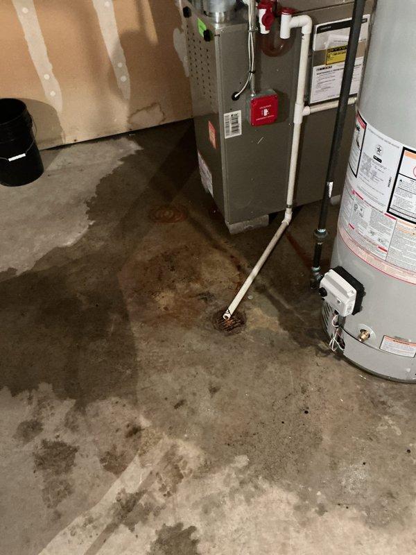 Responded to water leak concern in basement utility area where excessive water had been appearing near furnace and recently installed water heater for 4-5 days. Upon inspection, found extensive water staining and pooling on concrete floor throughout mechanical room. Investigated both the new water heater installed on 11/7/25 and HVAC condensation system as potential sources. Documented conditions showing dark discoloration and moisture damage across floor surface, with water accumulation most prominent in center area between furnace unit and water heater. Examined all plumbing connections, drain lines, and condensate discharge points. Photographed wet conditions and equipment for documentation purposes. Determined source of water intrusion and provided recommendations for remediation in fifty-year-old home.