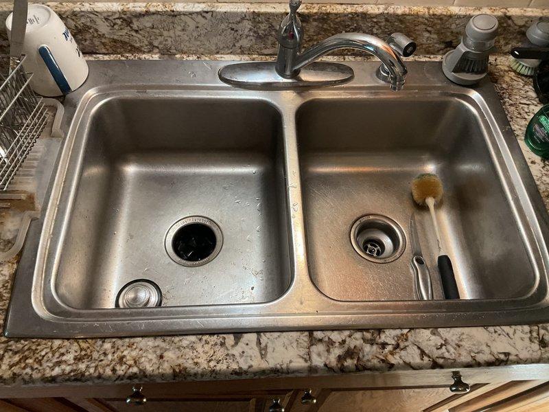 Successfully snaked the kitchen drain line to clear the blockage and restore proper drainage. Accessed the system through the P-trap assembly beneath the double-basin sink, navigating past the garbage disposal connection. Upon completion, verified water flow through both basins and confirmed the drain system was functioning properly with no leaks at the connections.
