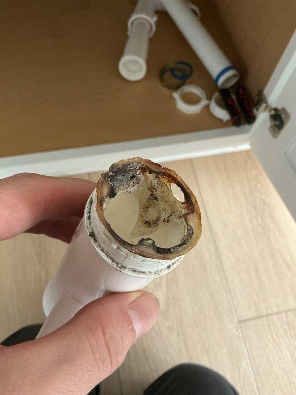 Responded to warranty concern regarding previous kitchen sink valve repair. Upon inspection, determined the active leak was not related to the prior valve replacement work. Investigation revealed severe mineral buildup and corrosion within existing PVC drain piping beneath the kitchen sink, which was the actual source of the water leak. The deteriorated pipe sections showed significant scale accumulation and rust-colored deposits that had substantially reduced the interior diameter and compromised the integrity of the drain system. Disassembled affected PVC drainage components including straight sections, elbow joints, and T-connectors to assess extent of damage. Documented the corroded pipe condition showing heavy mineral deposits on interior walls. Explained findings to customer that the leak originated from the deteriorated drain piping system rather than the previously completed valve repair work, confirming the prior repair remained intact and functional.