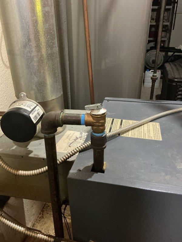 Responded to service call for 28-year-old hot water boiler in basement with reported leak occurring during operation. Upon inspection, identified active water leak at pipe connections and fittings. Examined pressure gauge readings, inspected flexible conduit connections, and assessed condition of copper piping, brass fittings, and shut-off valves. Documented equipment condition showing age-related wear on metal components and evidence of moisture accumulation on surrounding ductwork and tanks. Evaluated overall system integrity including electrical junction box connections and mechanical components to determine source of leak and necessary repairs.