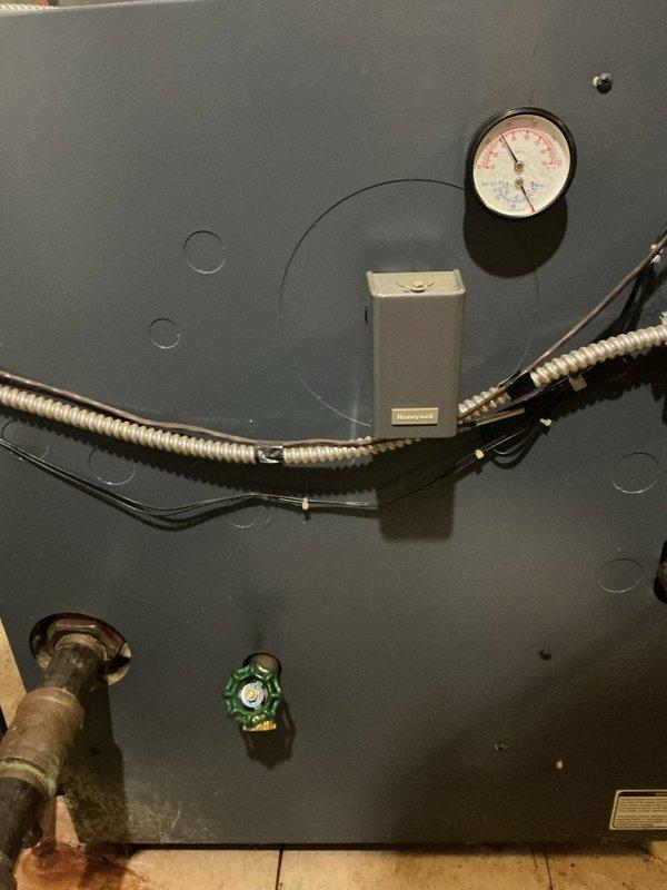 Responded to service call for 28-year-old hot water boiler in basement with reported leak occurring during operation. Upon inspection, identified active water leak at pipe connections and fittings. Examined pressure gauge readings, inspected flexible conduit connections, and assessed condition of copper piping, brass fittings, and shut-off valves. Documented equipment condition showing age-related wear on metal components and evidence of moisture accumulation on surrounding ductwork and tanks. Evaluated overall system integrity including electrical junction box connections and mechanical components to determine source of leak and necessary repairs.