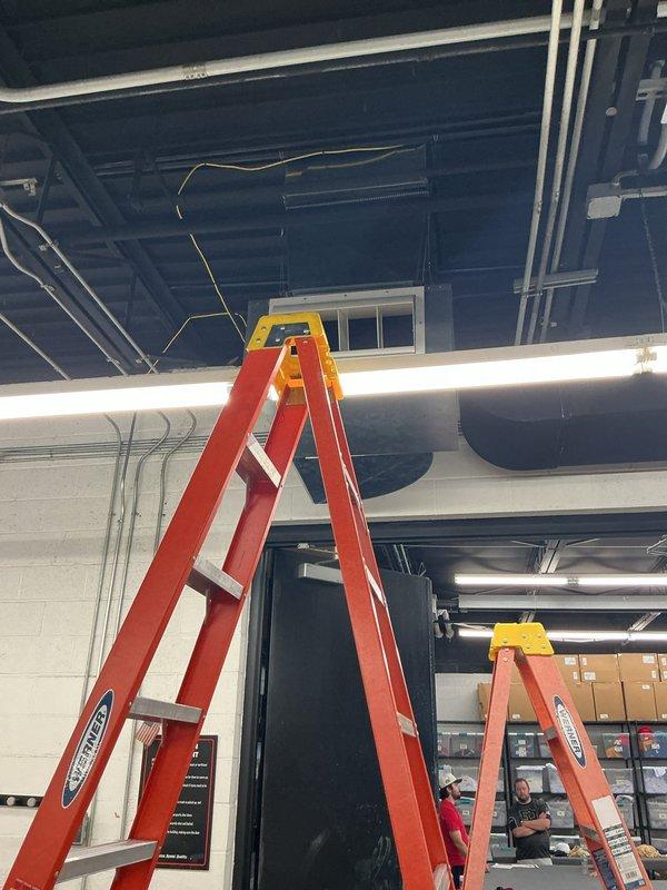 Installed commercial rooftop DOAS unit on knock-down curb at bearing wall location. Set and secured curb for roofer flashing and deck opening, extended gas line from roof main, completed electrical and control connections, and fabricated W-configuration supply drop with three legs and grilles. Installed and programmed CaptiveAire zone control panel, resolving communications fault during system configuration and startup.