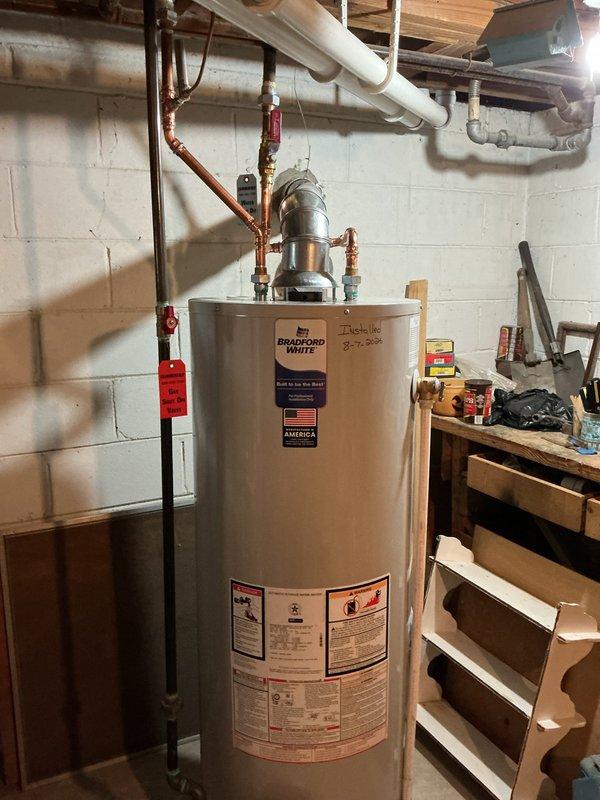 Responded to complaint of lukewarm water and performed complete 40-gallon Bradford White water heater replacement in basement utility area. Removed existing failed water heater unit, including disconnection of gas control valve, burner assembly, and associated components. Installed new 40-gallon tank with proper copper supply line connections, red-handled shut-off valves, and black gas piping. Configured all top-mounted plumbing connections and verified proper venting through existing infrastructure. Installed required drip pan beneath unit to maintain compliance with municipal code requirements. Tested all connections for leaks, verified proper gas flow to burner assembly, and confirmed water heater operation at appropriate temperature settings. Unit installed against concrete block wall with adequate clearance for maintenance access.