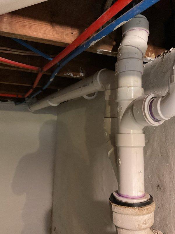Completed stack replacement in basement utility area. Removed existing deteriorated drain stack and installed new white PVC drainage system with proper venting configuration. New installation includes vertical stack with multiple horizontal branch connections utilizing appropriate fittings, elbows, and rubber gasket seals at all joints. Connected new PVC stack to existing drain connection at floor level. All work performed to code with secure mounting to concrete block wall. System tested and verified for proper drainage flow.