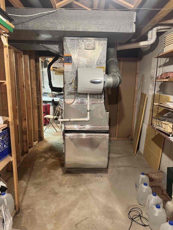 Completed installation of 3-ton air conditioning system with new evaporator coil in rear yard location. Indoor furnace unit fitted with coil and humidifier reconnection in basement utility area, with all ductwork properly connected and sealed. Outdoor Lennox condenser unit positioned on concrete pad against exterior wall with refrigerant lines run, electrical connections completed, and system tested for proper operation.