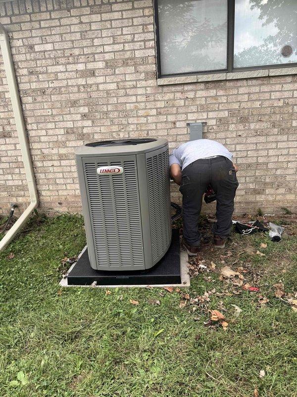 Completed installation of 3-ton air conditioning system with new evaporator coil in rear yard location. Indoor furnace unit fitted with coil and humidifier reconnection in basement utility area, with all ductwork properly connected and sealed. Outdoor Lennox condenser unit positioned on concrete pad against exterior wall with refrigerant lines run, electrical connections completed, and system tested for proper operation.
