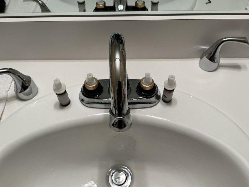 Responded to customer report of leaking bathroom faucet on upper level. Upon inspection, identified worn valve stems on chrome two-handle faucet assembly causing water leak. Removed existing deteriorated valve stems and installed new Moen replacement valve stem cartridges with brass collars. Tested hot and cold water controls for proper operation and verified complete leak elimination. Faucet now functioning properly with no active leaks detected.