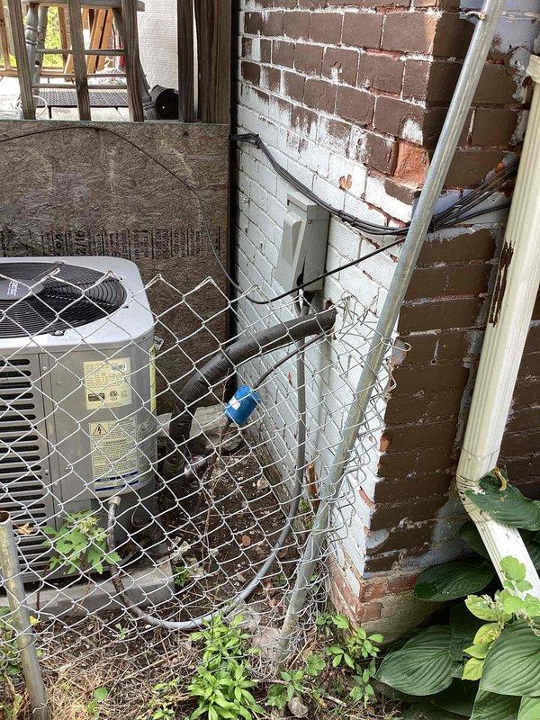 Conducted comprehensive site evaluation for complete HVAC system replacement at residential property. Assessed existing indoor air handler and ductwork configuration in basement mechanical room, documenting current plenum connections, galvanized ductwork condition, and furnace setup. Evaluated outdoor condensing unit positioned against building exterior behind chain-link fencing, noting equipment age, clearance requirements, and electrical service routing along brick wall. Photographed all existing equipment and installation conditions to provide accurate system sizing recommendations and replacement specifications for new central air conditioning system.