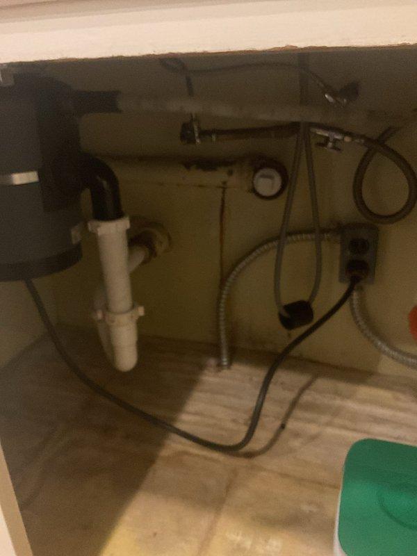 Responded to callback for dishwasher drainage issue where water was not properly evacuating from the appliance. Upon inspection of the under-sink plumbing system, examined the garbage disposal unit, drain connections, and dishwasher discharge line for potential blockages or improper drainage. Inspected all PVC trap assemblies, flexible hoses, and connection points beneath the kitchen sink for leaks or obstructions that could impede proper water flow from the dishwasher. Documented existing water staining on flooring beneath cabinet, indicating previous moisture issues. Verified all plumbing connections to disposal unit and drain system for proper installation and function.