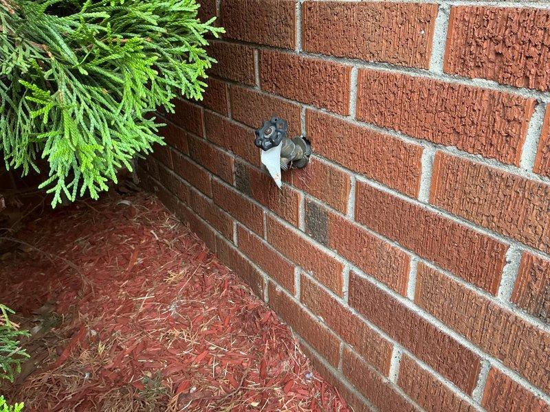 Replaced two exterior hose bibs as specified in the estimate. The first spigot was installed on an exterior brick wall with white PVC stub-out and dark valve handle, while the second featured a brass or copper pipe assembly with blue four-spoke wheel valve handle at an interior brick corner. Both installations were completed with proper mounting and secure connections to existing water supply lines.