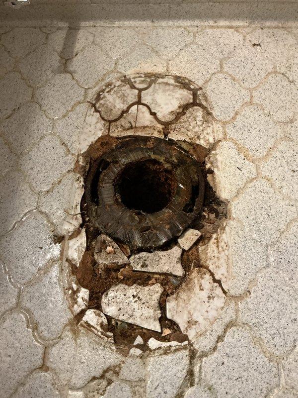 Coordinated with city utilities for water main shutoff to facilitate meter repairs and toilet installation. Replaced deteriorated floor drain assembly showing extensive corrosion and surrounding floor damage with broken tile and concrete fragments. Addressed water-damaged areas around drain perimeter exhibiting brown discoloration and structural deterioration. Completed toilet installation and restored water service following meter repair work. All plumbing connections tested and verified operational upon completion.