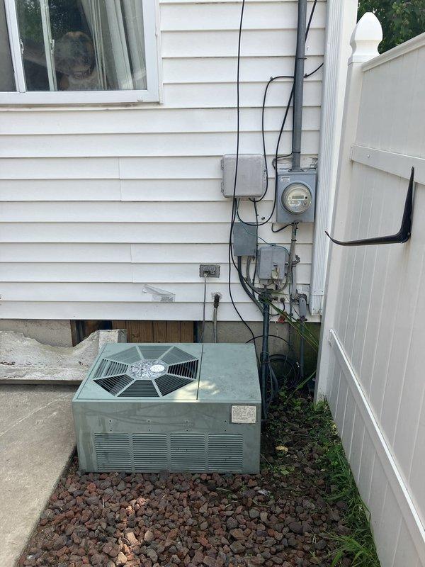 Responded to service call for 32-year-old air conditioning system experiencing loud operational noise during startup and shutdown, along with vibration noise during runtime. Upon arrival, inspected 1994-era condensing unit located in side yard between structures, mounted on concrete pad with lava rock landscaping. Unit was still providing cooling but exhibited signs of significant age-related wear consistent with equipment nearing end of service life. Documented existing installation including electrical service connections, meter configuration, and current equipment positioning. Performed comprehensive evaluation of condensing unit cabinet, fan assembly with protective guard, compressor operation, and mounting stability. Assessed noise sources related to aging mechanical components, worn motor bearings, and potential compressor issues typical of three-decade-old equipment. Photographed current installation showing unit placement, electrical infrastructure, surrounding clearances, and 