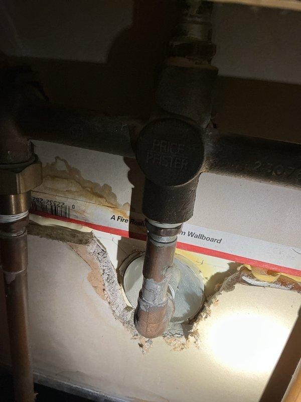 # Bathtub Hot Water Valve Leak Diagnosis and Shower Head Replacement Quote

Responded to service call for leaking hot water valve on bathtub fixture. Performed comprehensive diagnostic inspection of bathroom plumbing system. Identified aging Price Pfister valve assembly with deteriorated internal components causing active leak at hot water control. Inspected surrounding plumbing infrastructure beneath fixture, noting corrosion and water staining on pipe connections and cabinet surfaces consistent with prolonged moisture exposure.

Examined shower and tub area, documenting condition of existing fixtures including chrome showerhead with flexible metal hose attachment, clear plastic valve handles showing age-related discoloration, and tub spout. Noted significant mineral deposits, lime scale buildup on shower hose, and extensive rust staining on tub surface, wall tiles, grout lines, and drain assembly indicating long-term water quality issues and fixture deterioration.

Assessed shower he