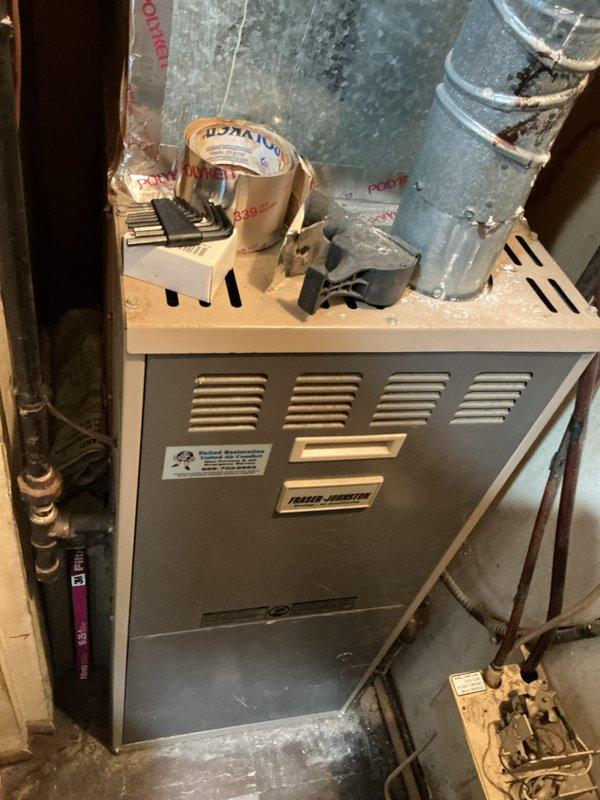 Conducted comprehensive assessment of existing 20-year-old furnace system located in utility closet for potential central air conditioning integration. Evaluated current HVAC infrastructure including furnace unit, existing ductwork configuration, and available space for AC component installation. Documented equipment specifications, duct routing through basement area, and structural considerations necessary for complete system upgrade. Photographed furnace unit with visible manufacturer labeling and existing metallic supply duct system to support estimate preparation for full HVAC system installation.