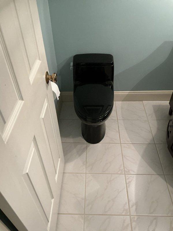 Responded to a water leak at the base of a main floor toilet in a thirty-year-old home. Upon inspection, found the leak had been ongoing for two days and was isolated to a single black one-piece toilet installed on ceramic tile flooring. Assessed the wax ring seal and flange connection as the likely source of the leak. Removed and reset the toilet, replaced the wax ring seal, inspected the closet flange for damage or deterioration, and secured all mounting bolts to proper torque specifications. Tested the toilet for proper operation and verified no further leakage at the base. Documented the completed repair with photographs showing the toilet installation and surrounding bathroom area.