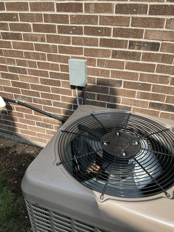 Completed Gold AC Inspection on a 2-year-old residential air conditioning system with outdoor condenser unit located in backyard and air handler in basement. Performed comprehensive visual inspection of condenser unit, verified fan operation and protective grille integrity, inspected refrigerant line connections, electrical disconnect box, and conduit routing along exterior wall. System found to be in normal operating condition with all components functioning properly at time of inspection.