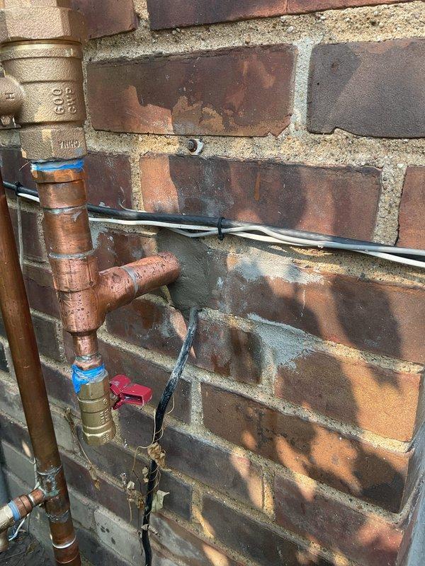 Responded to service call for cracked irrigation fitting on exterior copper plumbing assembly. Upon inspection, identified compromised plastic coupling connection on vertical supply line running along brick wall exterior. Replaced failed irrigation fitting and verified all connections were secure, including brass shutoff valve and hose bib assembly. System tested and confirmed operational with no leaks detected.