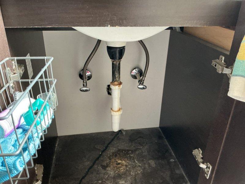 Responded to a clogged bathroom sink drain in a 70-year-old residence. Upon inspection, accessed the vanity cabinet and examined the plumbing assembly, including the PVC drain pipe, P-trap connections, and chrome supply lines. Evidence of previous water staining was noted on the cabinet floor, indicating past moisture issues. Cleared the localized blockage in the drain line, verified proper water flow and drainage, and confirmed all connections were secure with no active leaks present.