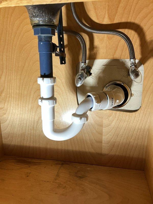 Completed drain line repair beneath kitchen sink. Removed and replaced deteriorated P-trap assembly with new white PVC piping and fittings, ensuring proper trap configuration for effective drainage and sewer gas prevention. Installed new drain tailpiece with threaded connection to accommodate sink basket strainer. Verified flexible braided water supply line connections to shut-off valve and faucet supply shank, confirming secure fittings without leaks. Tested entire drain assembly for proper flow and checked all connections under pressure. System operating correctly with no leaks detected at drain connections or supply line fittings.
