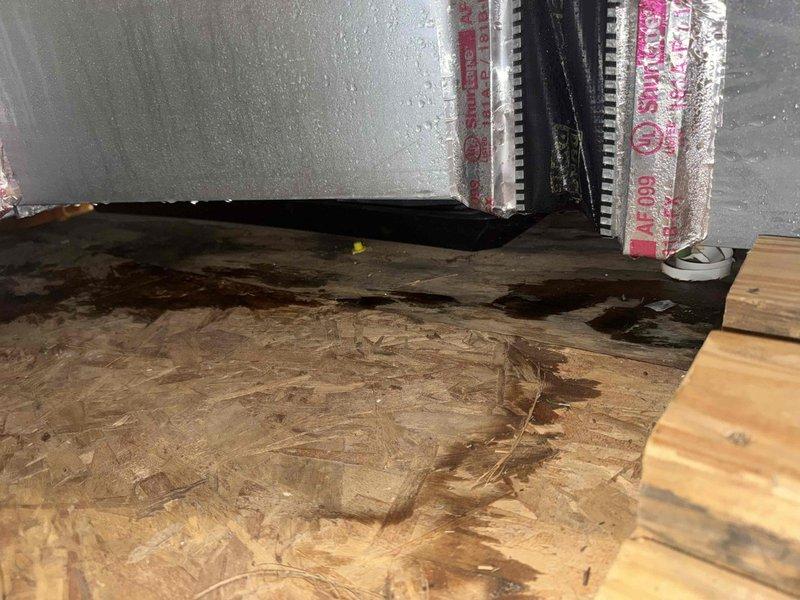 Responded to no-cooling call on 3-year-old attic-mounted slim tech AC unit with history of moisture-related shutdowns and previous motherboard/thermostat replacement. Upon inspection, found extensive water damage to attic floor surrounding air handler, with visible dark staining across multiple OSB panels indicating ongoing condensation issues. Confirmed inadequate or missing insulation on refrigerant lines and condensate management problems causing moisture accumulation on safety sensors, resulting in unit lockout. Documented water damage patterns and uninsulated ductwork contributing to excessive condensation in attic environment. Advised immediate insulation of refrigerant lines, proper condensate drain routing, and evaluation of air handler installation to prevent continued moisture intrusion and potential system failure.