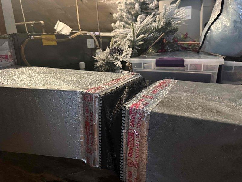 Responded to no-cooling call on 3-year-old attic-mounted slim tech AC unit with history of moisture-related shutdowns and previous motherboard/thermostat replacement. Upon inspection, found extensive water damage to attic floor surrounding air handler, with visible dark staining across multiple OSB panels indicating ongoing condensation issues. Confirmed inadequate or missing insulation on refrigerant lines and condensate management problems causing moisture accumulation on safety sensors, resulting in unit lockout. Documented water damage patterns and uninsulated ductwork contributing to excessive condensation in attic environment. Advised immediate insulation of refrigerant lines, proper condensate drain routing, and evaluation of air handler installation to prevent continued moisture intrusion and potential system failure.