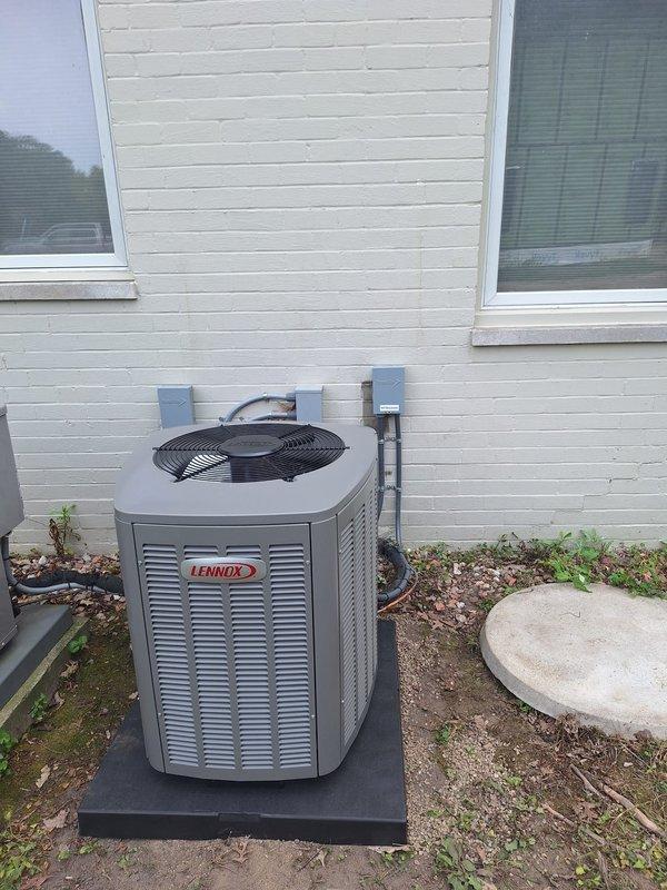 Completed installation of 2-ton Lennox air conditioning condenser unit and evaporator coil at residential property. Unit positioned in right yard area on protective pad against exterior wall with white horizontal siding. Installed electrical disconnect boxes, conduit, and refrigerant line connections from outdoor condenser to indoor coil. System reconnected and tested for proper operation following mechanical, electrical, and air conditioning permit requirements.
