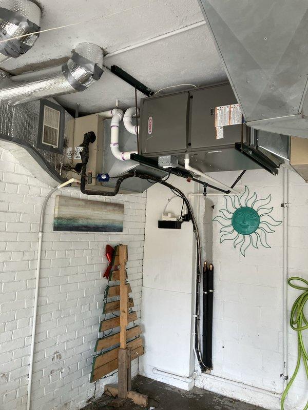 Completed installation of two furnace units and one water heater system in residential basement utility space. Mounted gray metal air handler unit to ceiling using reinforced metal brackets with reflective insulation wrapping for thermal efficiency. Installed white PVC condensate drain lines from equipment along wall to proper drainage point. Routed black flexible electrical conduit and silver metallic insulated supply ductwork from units to existing distribution system. Secured all ductwork and piping with appropriate metal clamps and straps per code requirements. Verified proper clearances around equipment for service access and safety compliance. System tested and operational upon completion.