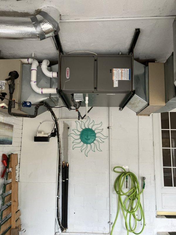 Completed installation of two furnace units and one water heater system in residential basement utility space. Mounted gray metal air handler unit to ceiling using reinforced metal brackets with reflective insulation wrapping for thermal efficiency. Installed white PVC condensate drain lines from equipment along wall to proper drainage point. Routed black flexible electrical conduit and silver metallic insulated supply ductwork from units to existing distribution system. Secured all ductwork and piping with appropriate metal clamps and straps per code requirements. Verified proper clearances around equipment for service access and safety compliance. System tested and operational upon completion.
