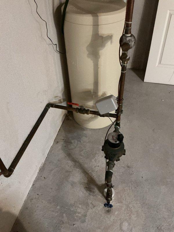 # Plumbing Service - Toilet/Urinal

Responded to service call for reported toilet issue on second floor of 26-year-old residential property. Upon arrival, conducted comprehensive plumbing system inspection to diagnose the problem. Investigation revealed that the reported toilet concern was not the primary issue requiring attention.

During diagnostic evaluation, discovered significant concerns with the water heater system located in the basement utility area. Identified water staining and discoloration on concrete floor surrounding water heater base, indicating active or previous moisture infiltration. Observed aged copper supply piping with visible tarnishing and oxidation throughout the plumbing assembly.

Documented deteriorating wall conditions adjacent to water heater installation, with vertical cracking visible on painted surface. Noted presence of collection cup positioned beneath lower pipe connections, suggesting known or suspected drip issues. Examined pressure relief valve a