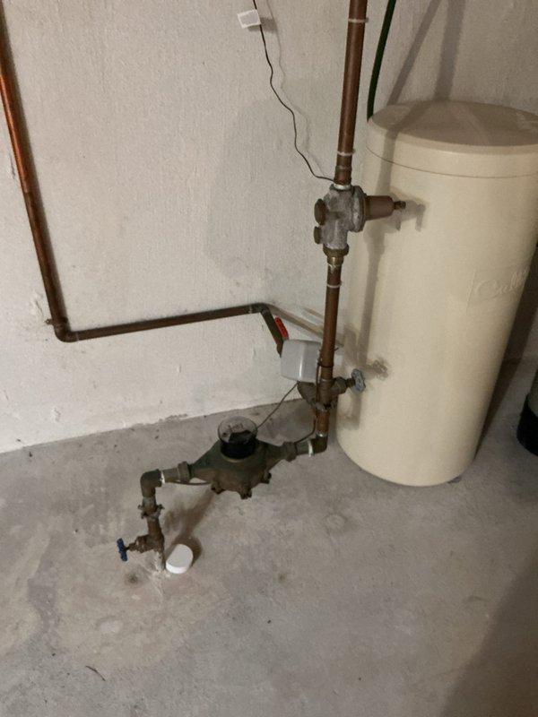 # Plumbing Service - Toilet/Urinal

Responded to service call for reported toilet issue on second floor of 26-year-old residential property. Upon arrival, conducted comprehensive plumbing system inspection to diagnose the problem. Investigation revealed that the reported toilet concern was not the primary issue requiring attention.

During diagnostic evaluation, discovered significant concerns with the water heater system located in the basement utility area. Identified water staining and discoloration on concrete floor surrounding water heater base, indicating active or previous moisture infiltration. Observed aged copper supply piping with visible tarnishing and oxidation throughout the plumbing assembly.

Documented deteriorating wall conditions adjacent to water heater installation, with vertical cracking visible on painted surface. Noted presence of collection cup positioned beneath lower pipe connections, suggesting known or suspected drip issues. Examined pressure relief valve a