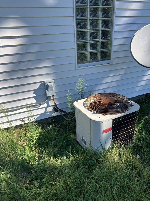 Conducted comprehensive site evaluation for new air conditioning system installation at residential property. Assessed existing 8-year-old furnace unit located in garage area, currently operating with Bryant brand outdoor condenser positioned on concrete pad against exterior wall with glass block window. Documented existing HVAC infrastructure including metal ductwork configuration, electrical disconnect box placement, and available installation space within confined utility area featuring wooden framing and concrete flooring. Evaluated outdoor unit placement considerations including overgrown vegetation surrounding current equipment and accessibility for new system installation. Photographed existing equipment conditions, ductwork routing, and available installation locations to develop accurate system specifications. Prepared detailed equipment recommendations and installation scope for complete air conditioning system addition to complement existing furnace operation.