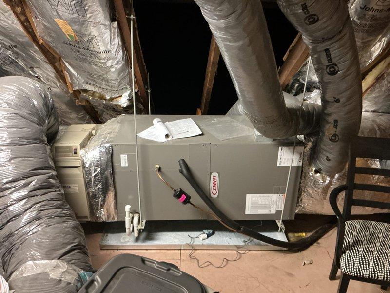 Responded to service call for non-operational five-year-old Carrier AC system providing no cooling to residence. Performed comprehensive system evaluation of both outdoor condensing unit and indoor air handler located in attic space. Assessed existing Lennox air handler installation with associated ductwork, refrigerant lines, and condensate management system. Evaluated exterior condensing unit condition, noting vegetation debris accumulation on refrigerant line set and surrounding infrastructure requiring clearance for proper system operation. Documented current equipment configuration including flexible duct distribution system with Johns Manville insulation and copper refrigerant piping with insulation jacket. Provided detailed estimate for complete HVAC system replacement including new outdoor condensing unit and compatible air handler to restore cooling capacity and system functionality. Captured photographic documentation of existing equipment condition, installation location, an