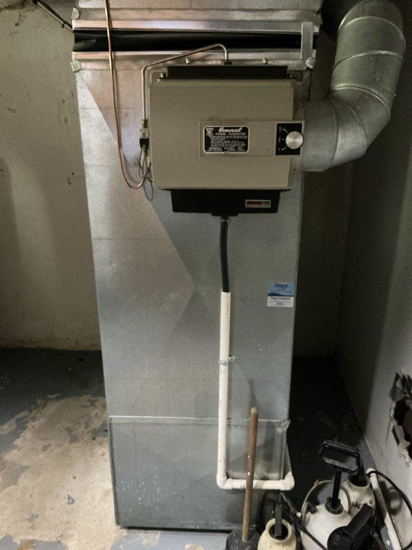 Completed full HVAC system replacement in basement utility room for medium-sized residential property (1500-3000 sq.ft.). Installed new Lennox combination air conditioning and natural gas furnace system configured as vertical upflow/downflow unit. System includes metallic ductwork with elbow connection, white metal plenum with angled bottom, copper refrigerant lines with brass fittings, PVC condensate drain line, and condensate pump with associated tubing connections. Unit mounted on concrete floor against concrete block wall with proper electrical connections and standard manufacturer specification labels installed.